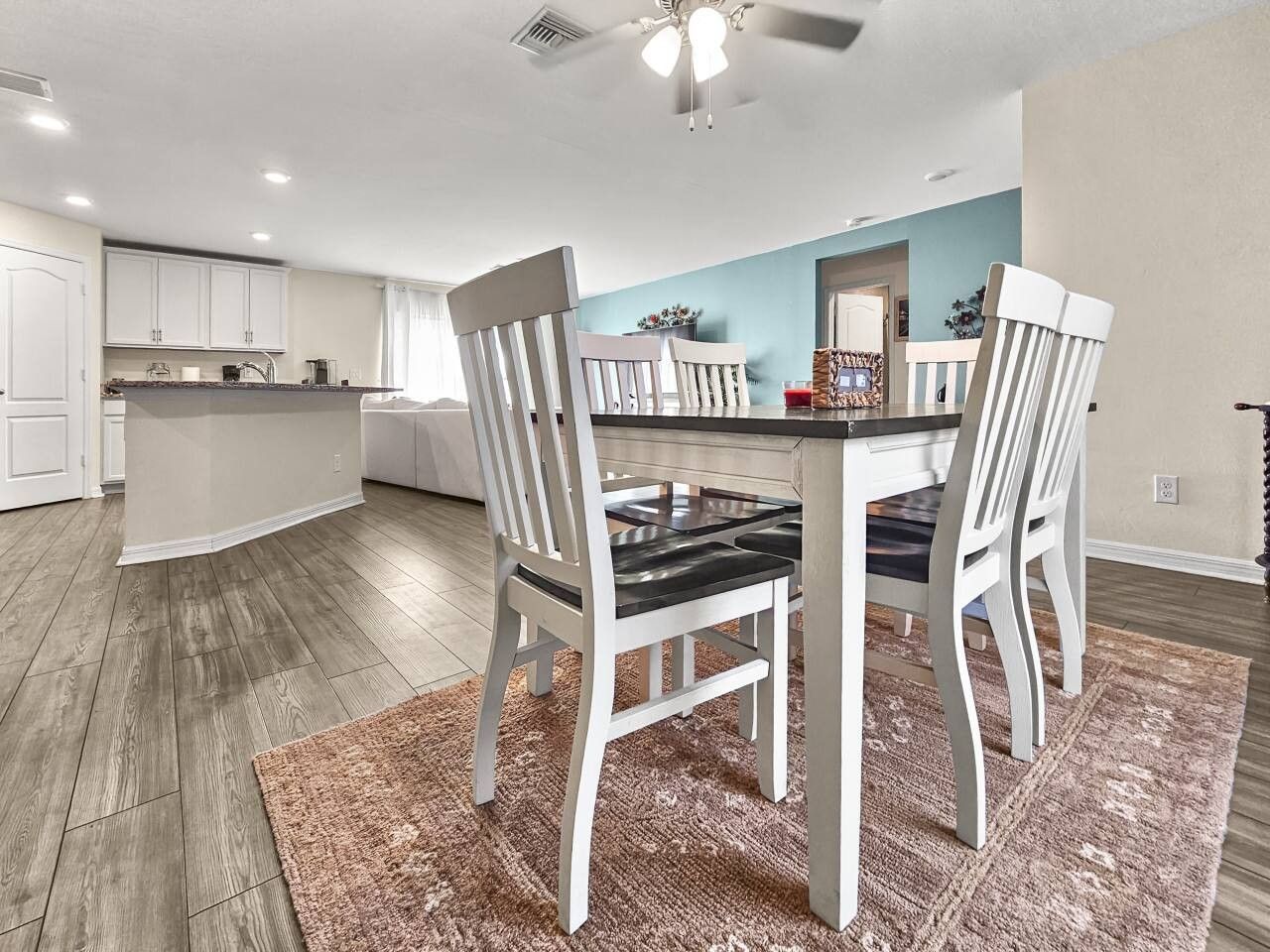 A modern kitchen with white cabinets, a dining area with a table and chairs, and a ceiling fan.