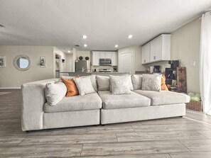 Una sala de estar moderna con un sofá modular, una cocina al fondo y un comedor.