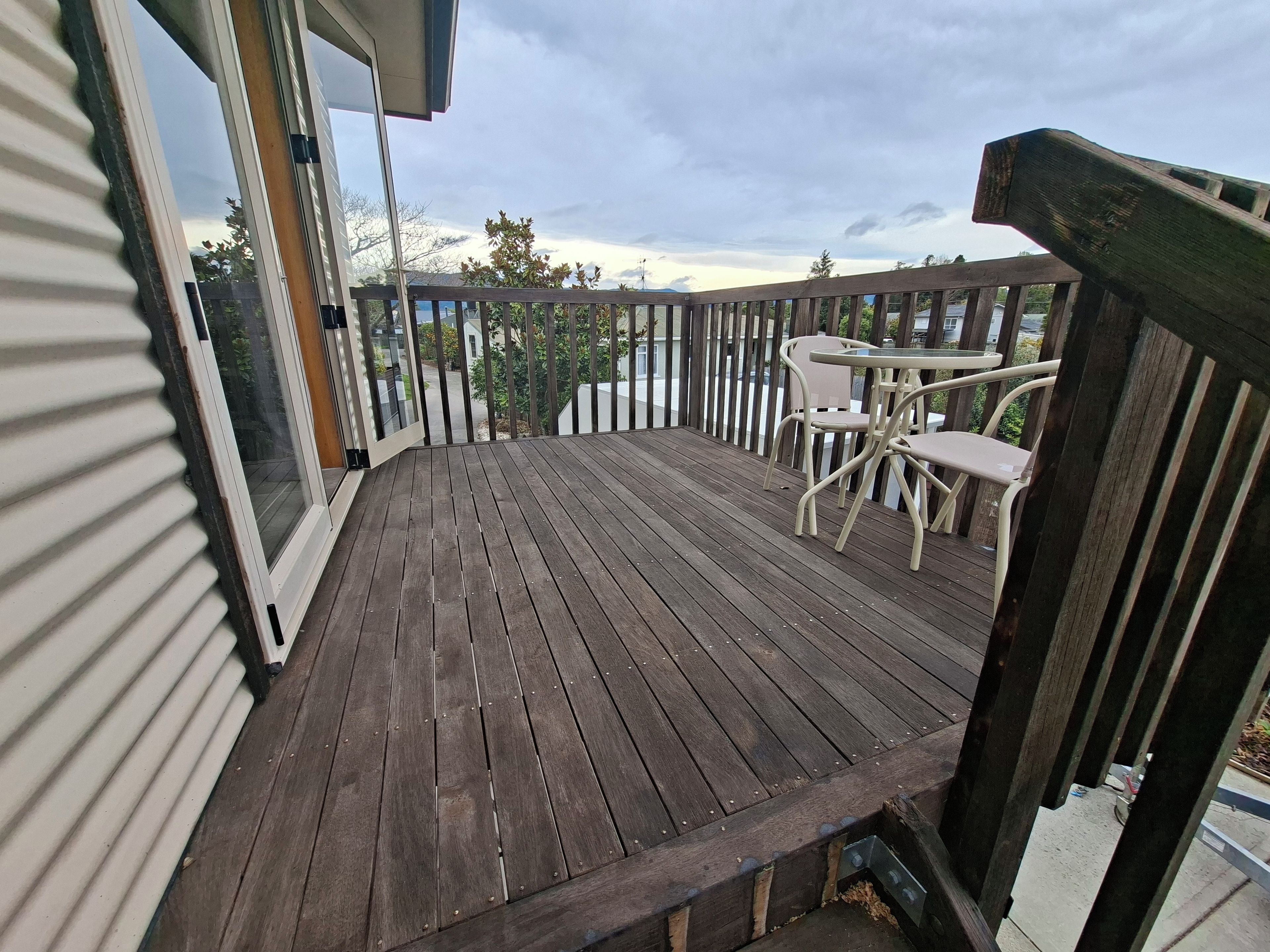 A wooden deck with a table and chairs, a railing, and a view of the surrounding area.