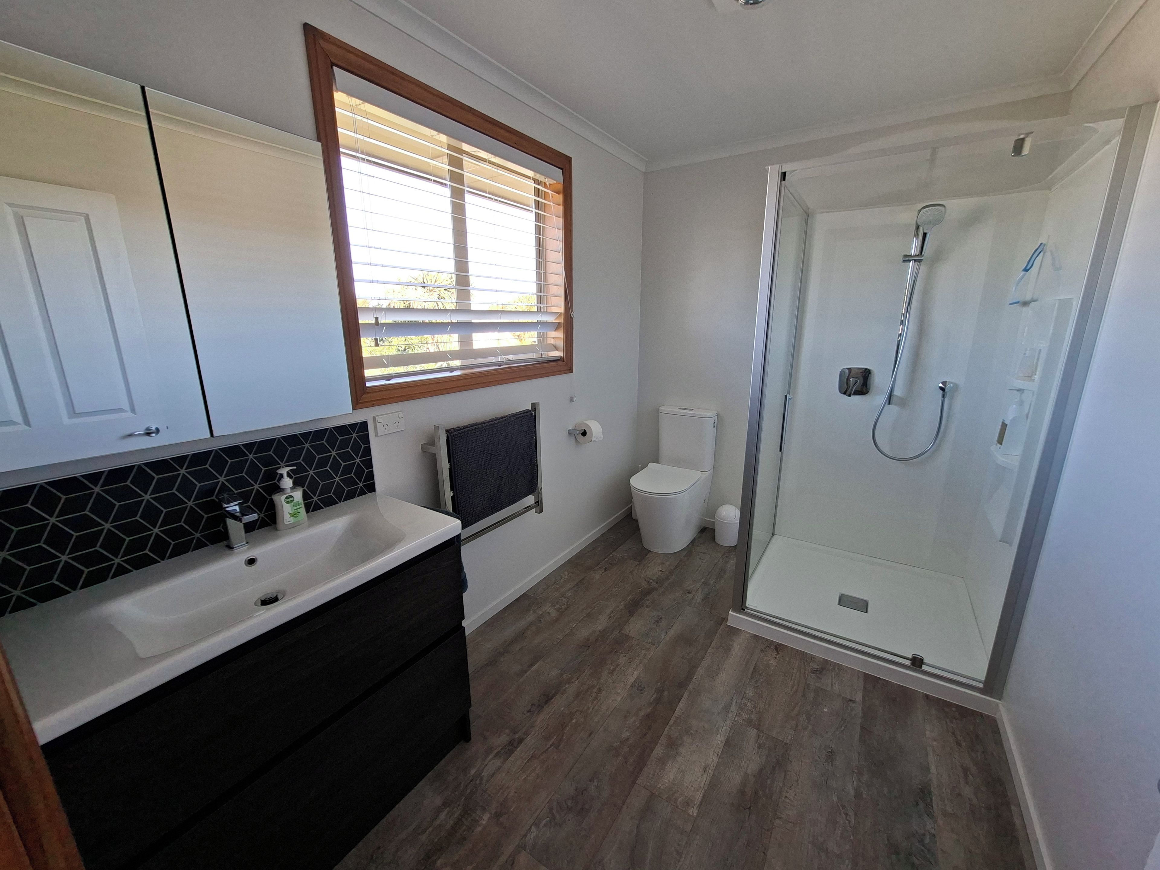 A bathroom with a shower, toilet, sink, and a window with blinds.
