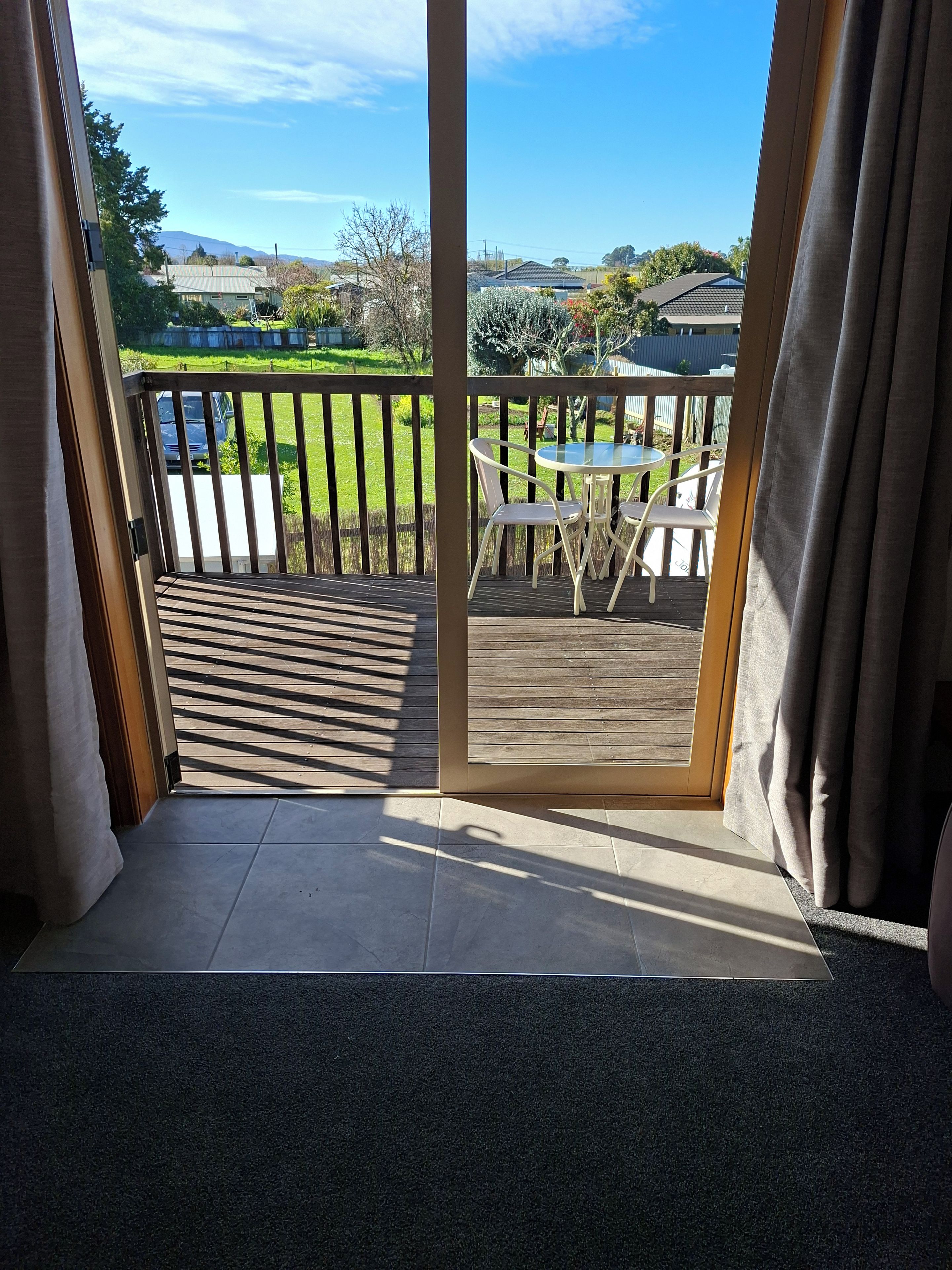Quarto com porta de vidro deslizante que dá para um deck externo com mesa e cadeiras.