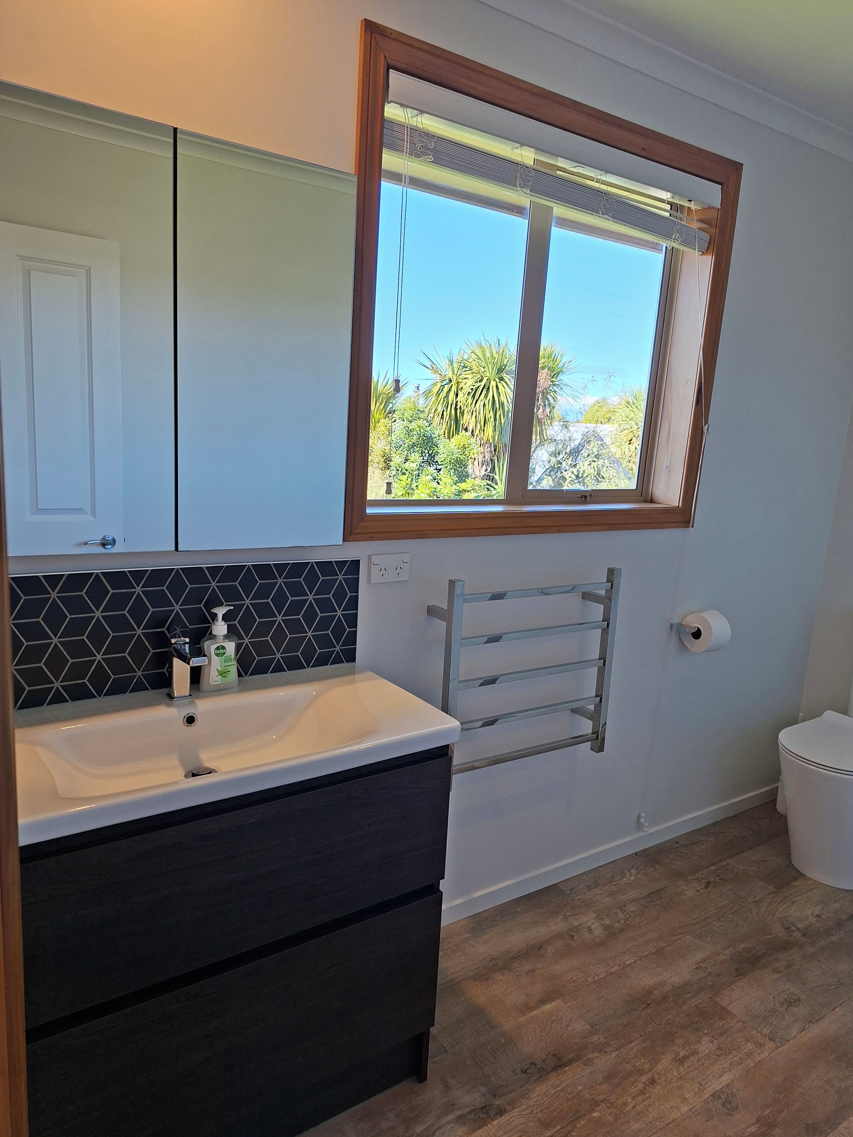 A bathroom with a white sink, dark cabinets, a towel rack, and a window with a view of greenery.