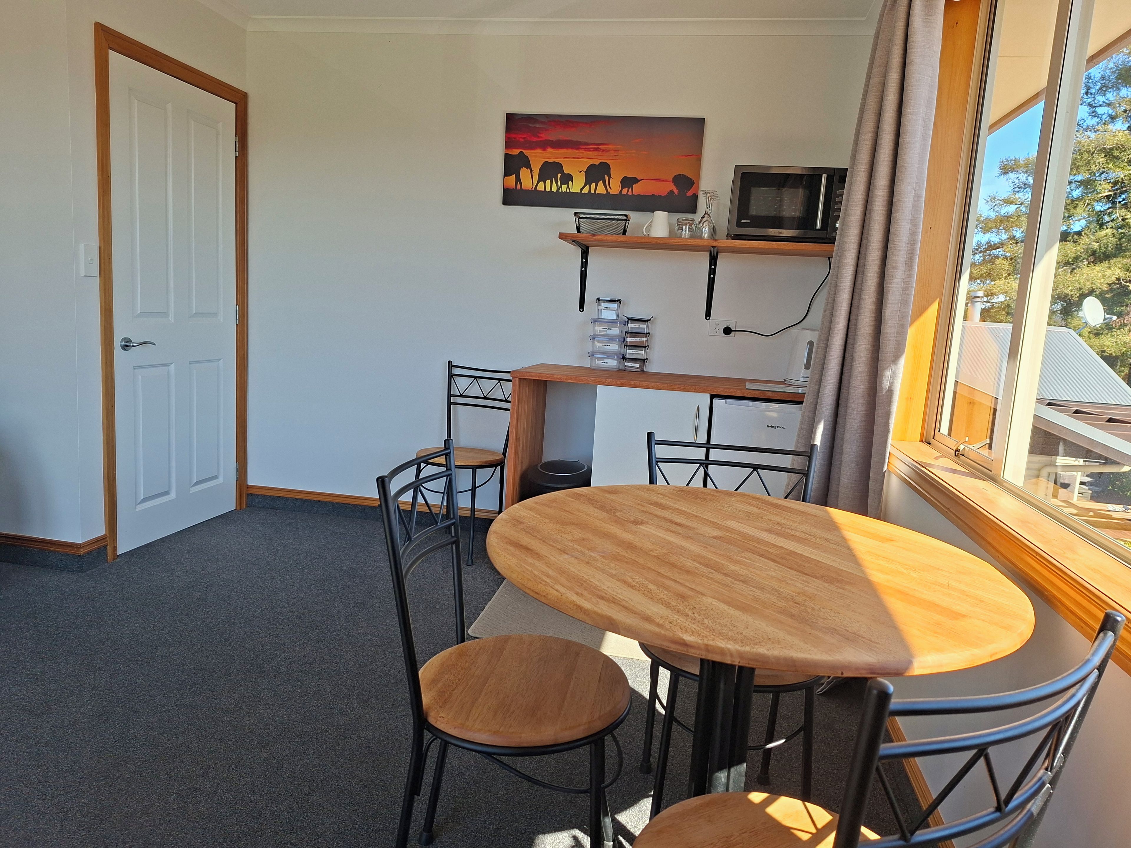 A room with a dining table, chairs, a microwave, and a painting on the wall.