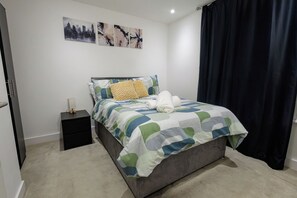 A neatly made bed with a striped bedspread, a pillow, and a rolled towel on a dark-colored mattress. - Stylish 2-Bed Apartment -Canary Wharf - Sleeps 5- Near City Airport & Westfields (London)