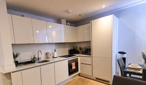 A modern kitchen with white cabinets, a sink, a stove, and a dining area with a table and chairs. - Stylish 2-Bed Apartment -Canary Wharf - Sleeps 5- Near City Airport & Westfields (London)