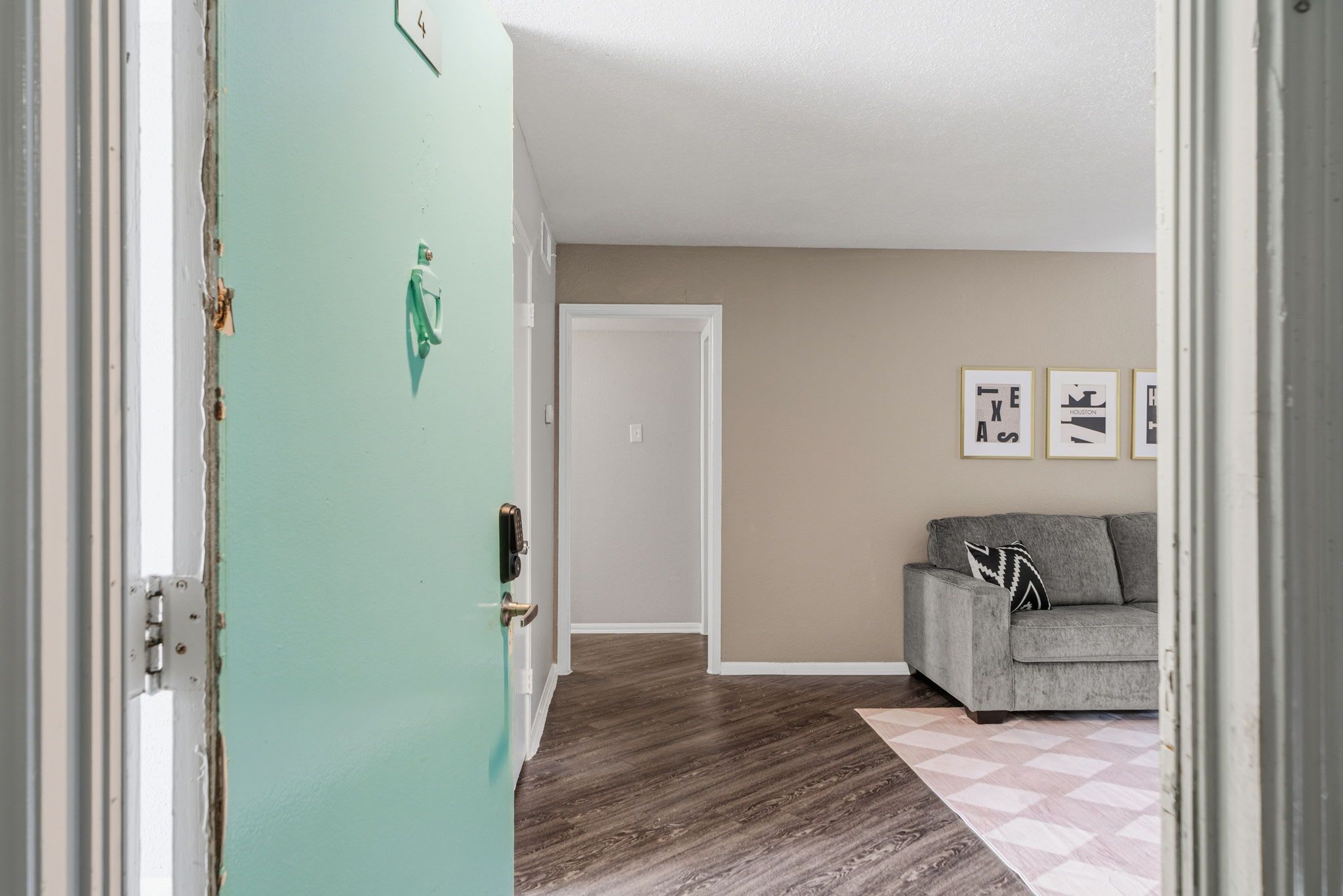 A room with a teal door, a grey sofa, a patterned rug, and framed pictures on the wall.