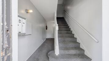 A staircase with a white handrail and carpeted steps leading to a door with a mailbox and a wall-mounted light fixture.