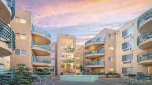 Un edificio a più piani con balconi, un cortile centrale con una fontana e un cielo al tramonto.