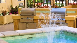 Ein Außenpoolbereich mit integriertem Grill und Wasserspiel.
