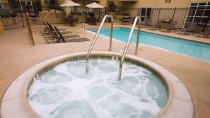 Ein Whirlpool mit Metallstufen, umgeben von Liegestühlen und Sonnenschirmen, neben einem Schwimmbecken.