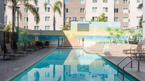 Una piscina con lettini e ombrelloni, circondata da un edificio con un murale raffigurante una spiaggia.