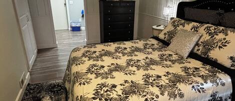 A bedroom with a bed, dresser, and a door leading to another room.