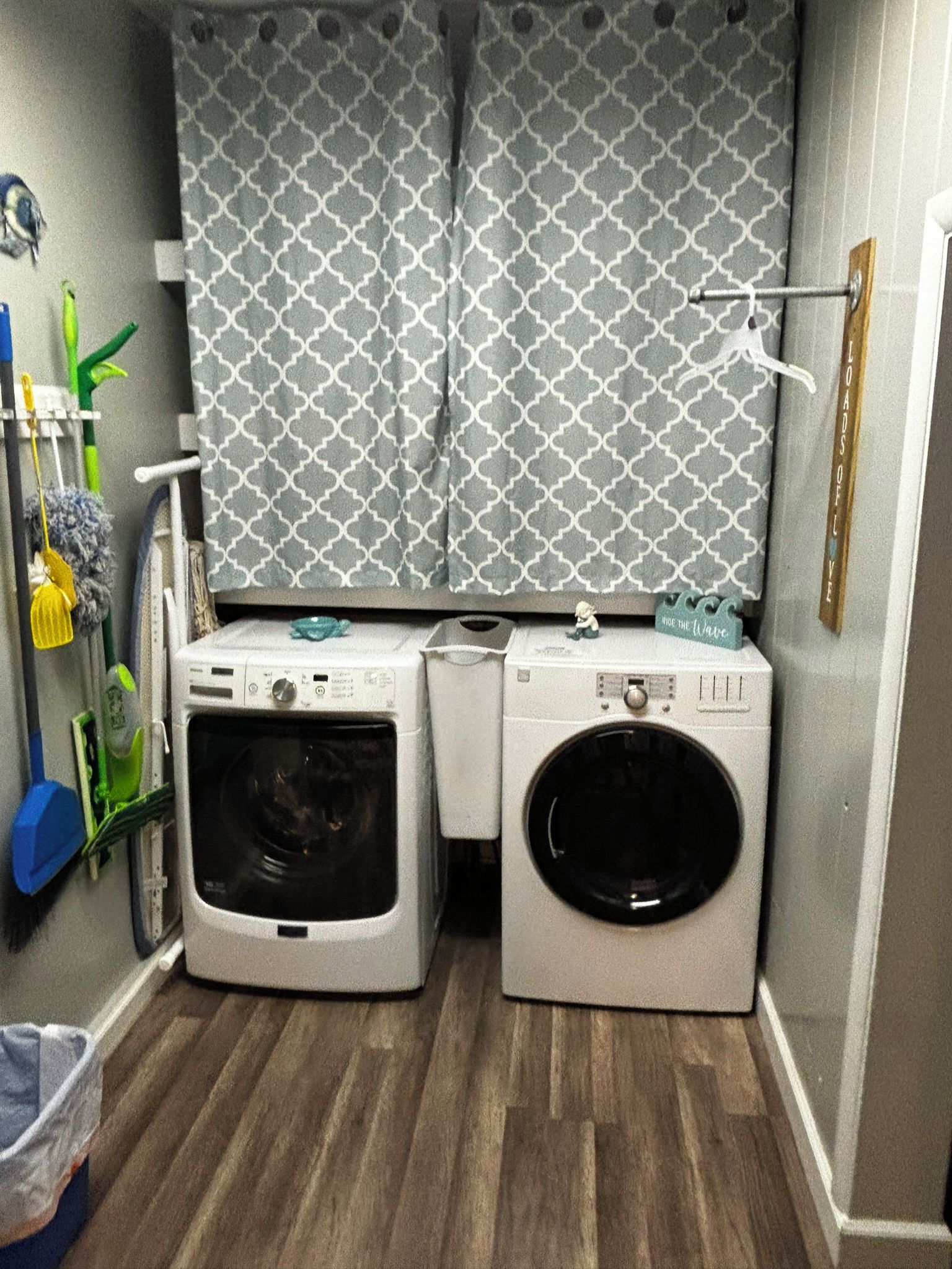 A compact laundry room with two front-loading washing machines, a drying rack, and a small shelf with a decorative item.