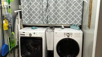 A compact laundry room with two front-loading washing machines, a drying rack, and a small shelf with a decorative item.