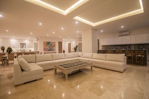 Una sala moderna con un sofá modular, una mesa de centro y una zona de cocina con taburetes de bar.