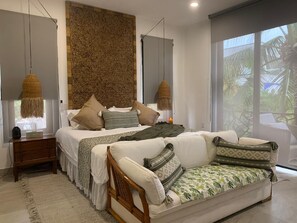 Quarto moderno com cama grande, sofá e vista para palmeiras.