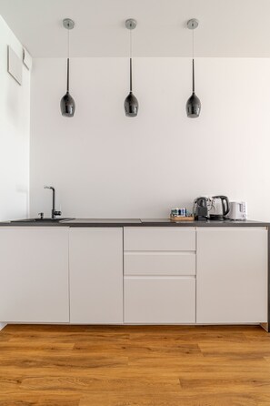 Eine moderne Küche mit weißer Arbeitsplatte, drei Pendelleuchten, einer Kaffeemaschine und einem Wasserkocher.
