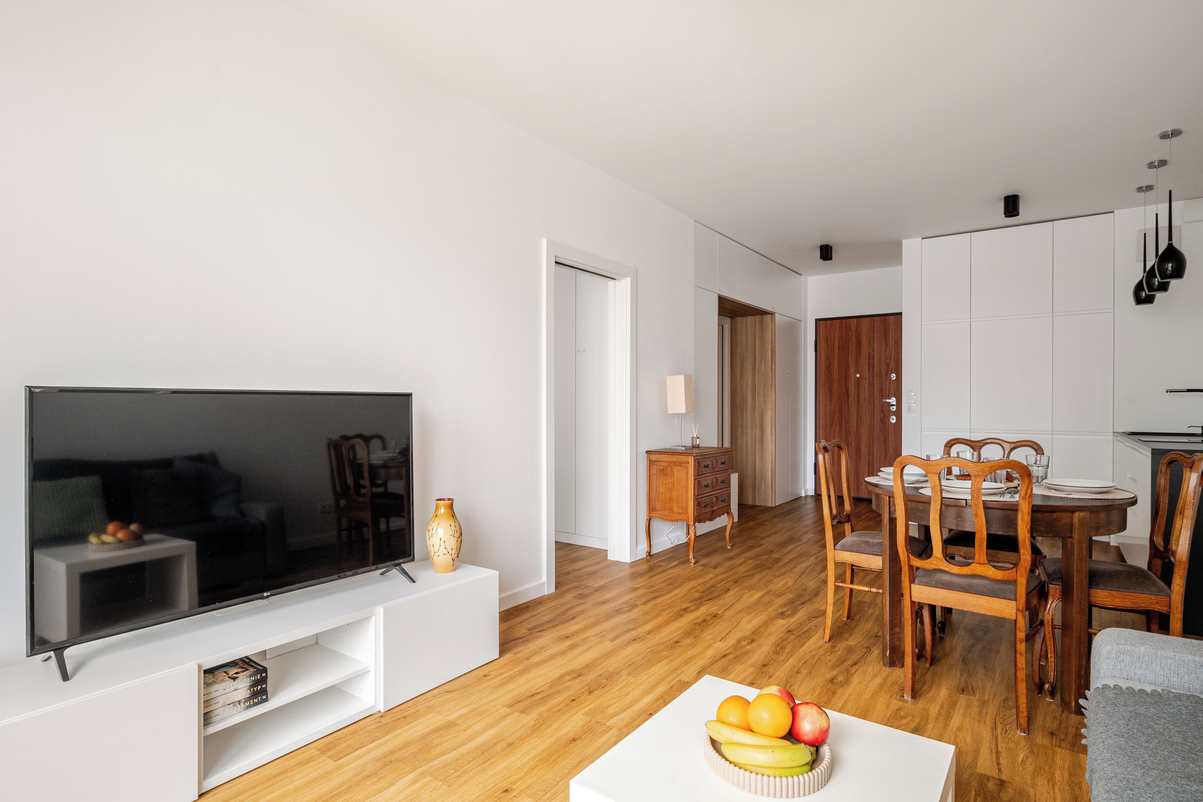 Ein modernes Wohnzimmer mit Flachbildfernseher, Esstisch aus Holz und Stühlen.