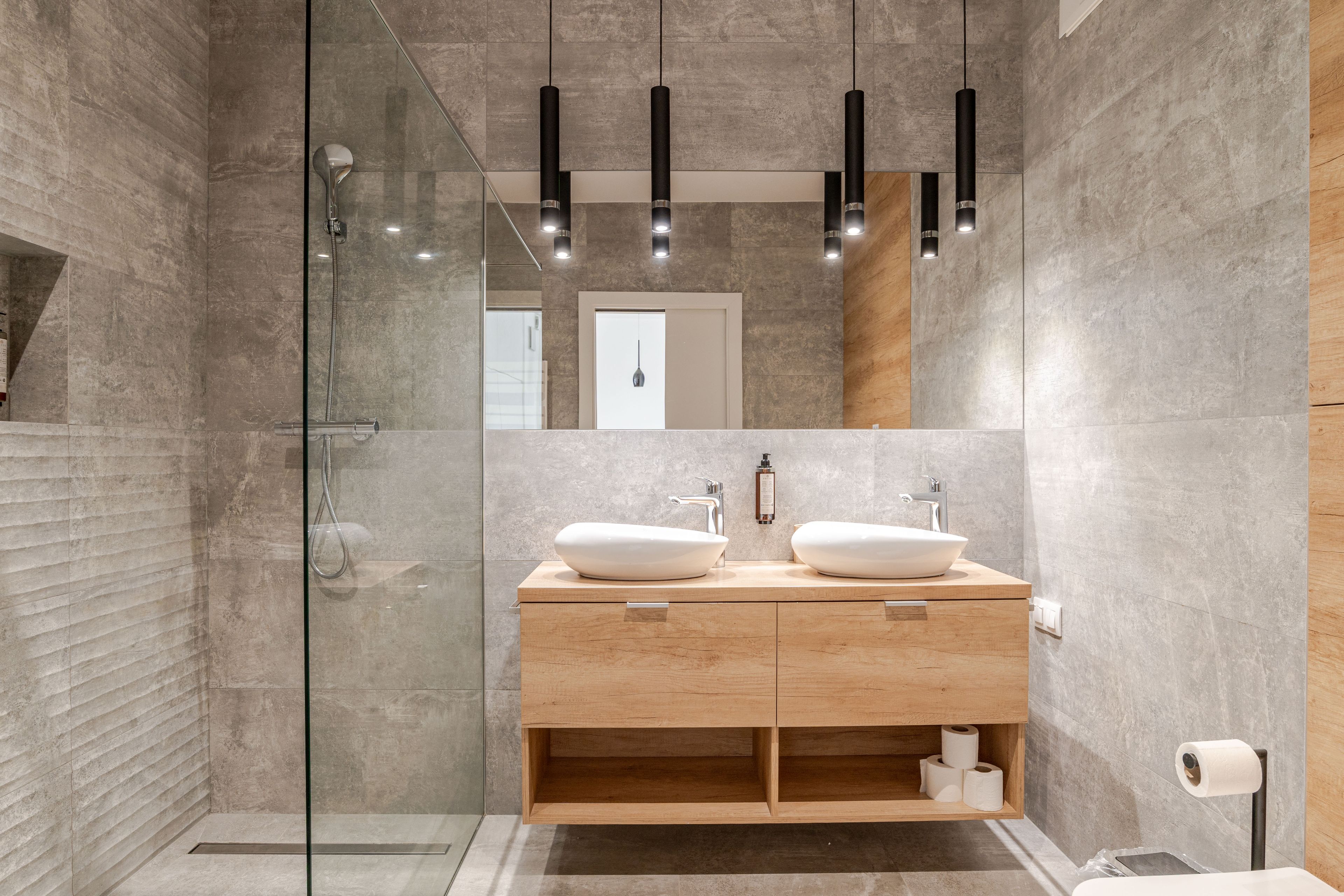 Ein modernes Badezimmer mit Duschkabine aus Glas, zwei Waschbecken und einem Holzwaschtisch.