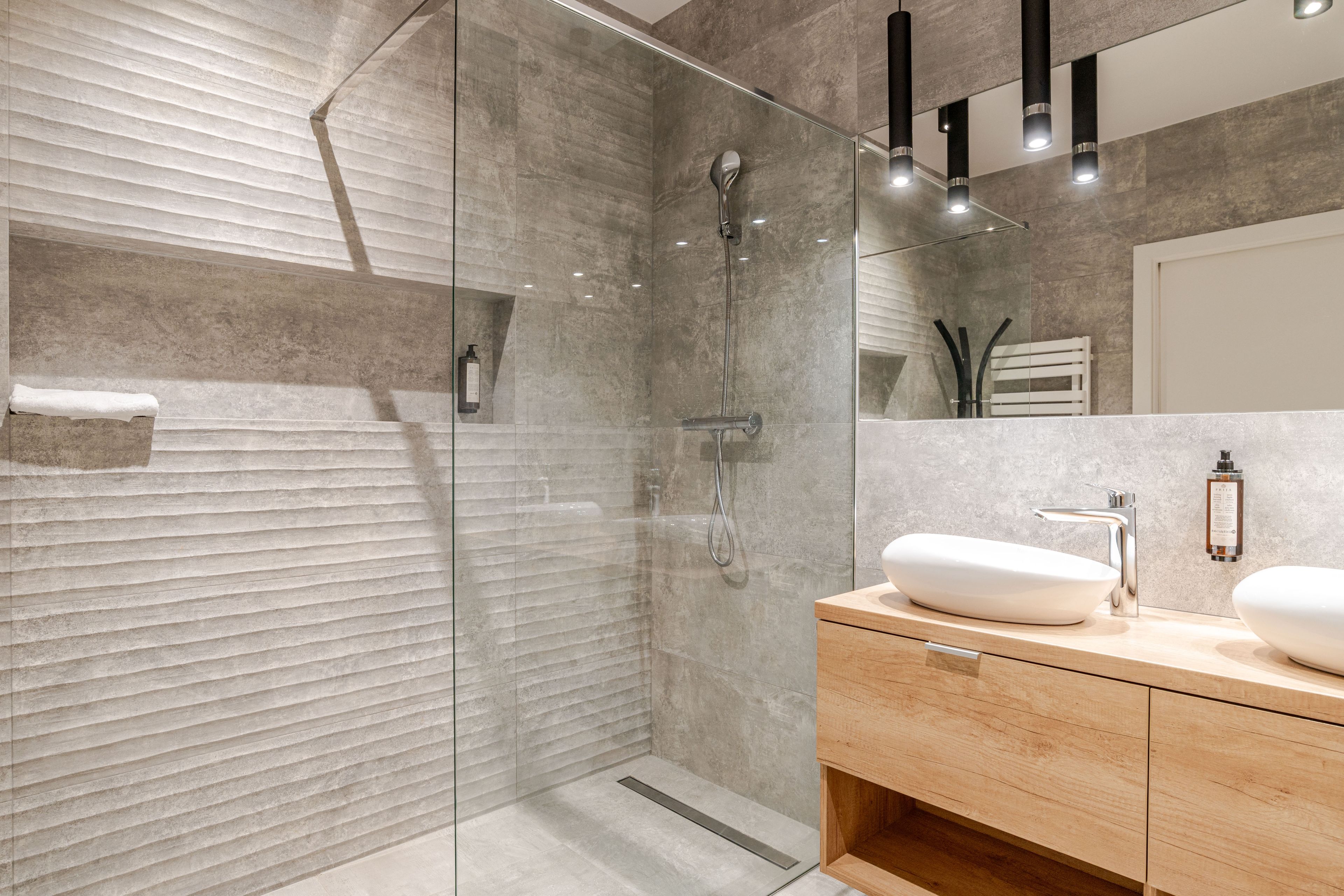 A modern bathroom with a glass-enclosed shower, a wooden vanity, and a large mirror.