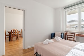 Quarto de hotel com uma cama, uma escrivaninha, uma cadeira e uma mesa de jantar.