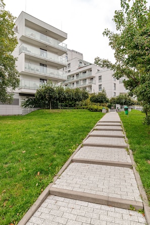 A pathway leading to a modern apartment building with multiple balconies and a grassy area. - Dereniowa 10 Apartment by StayFirst.pl (Warszawa)