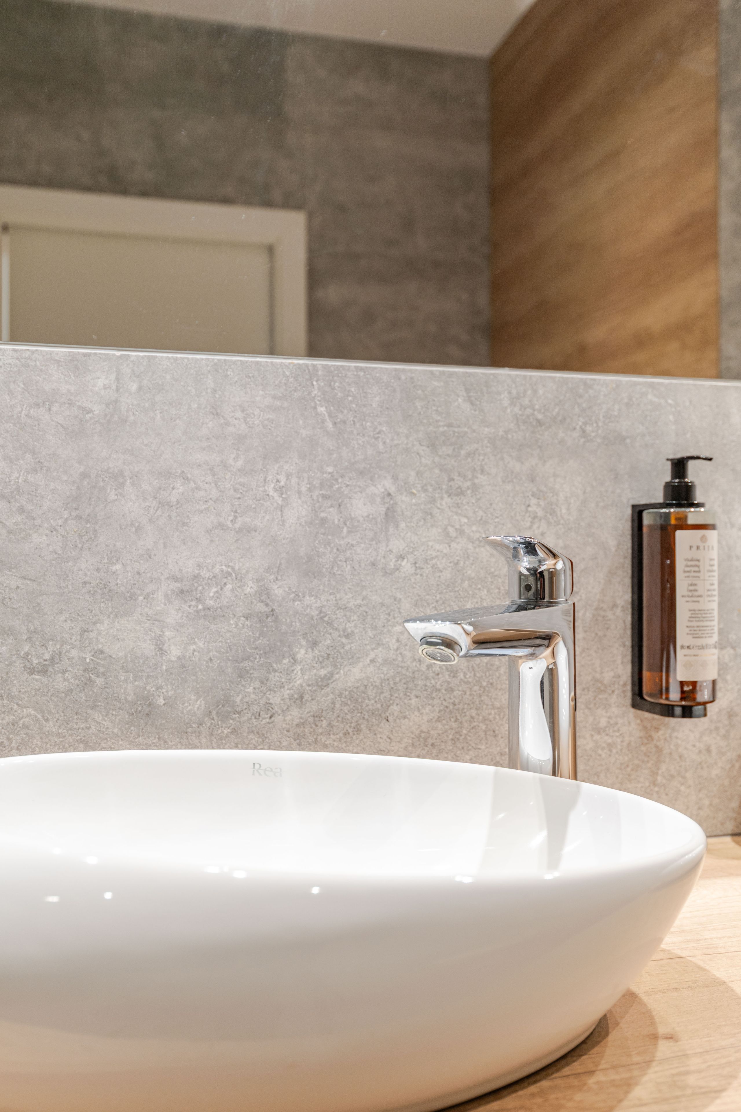 Un bagno con un lavandino bianco, un rubinetto cromato e una bottiglia di sapone per le mani a parete.