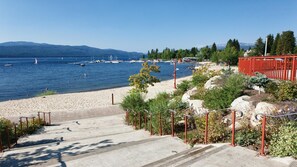 En betongtrappa som leder ner till en strand med båtar i vattnet och berg i bakgrunden.