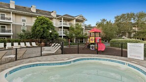 Ein Poolbereich mit Spielplatz für Kinder, Liegestühlen und einer umzäunten Terrasse.