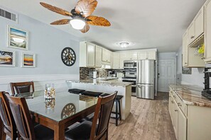 Una cocina moderna con una isla central, electrodomésticos de acero inoxidable y un ventilador de techo con aspas de madera.