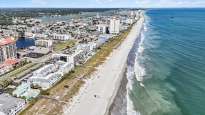 Vista aérea de una ciudad costera con playa, edificios y un muelle.