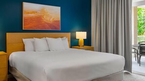 A hotel room with a bed, a nightstand with a lamp, a painting on the wall, and a view of the outdoors through a window.
