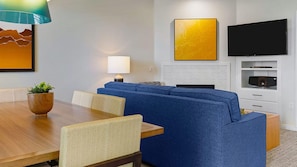 Una sala moderna con un sofá azul, una mesa de comedor de madera, una lámpara, un televisor de pantalla plana y una chimenea.