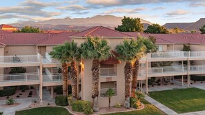 A multi-story hotel with balconies, palm trees, and a mountainous backdrop.