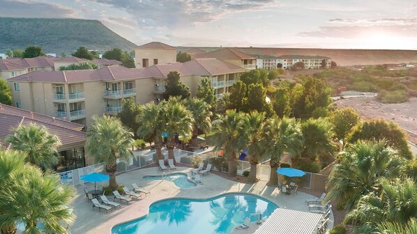 A resort with a swimming pool, palm trees, and a mountainous backdrop.
