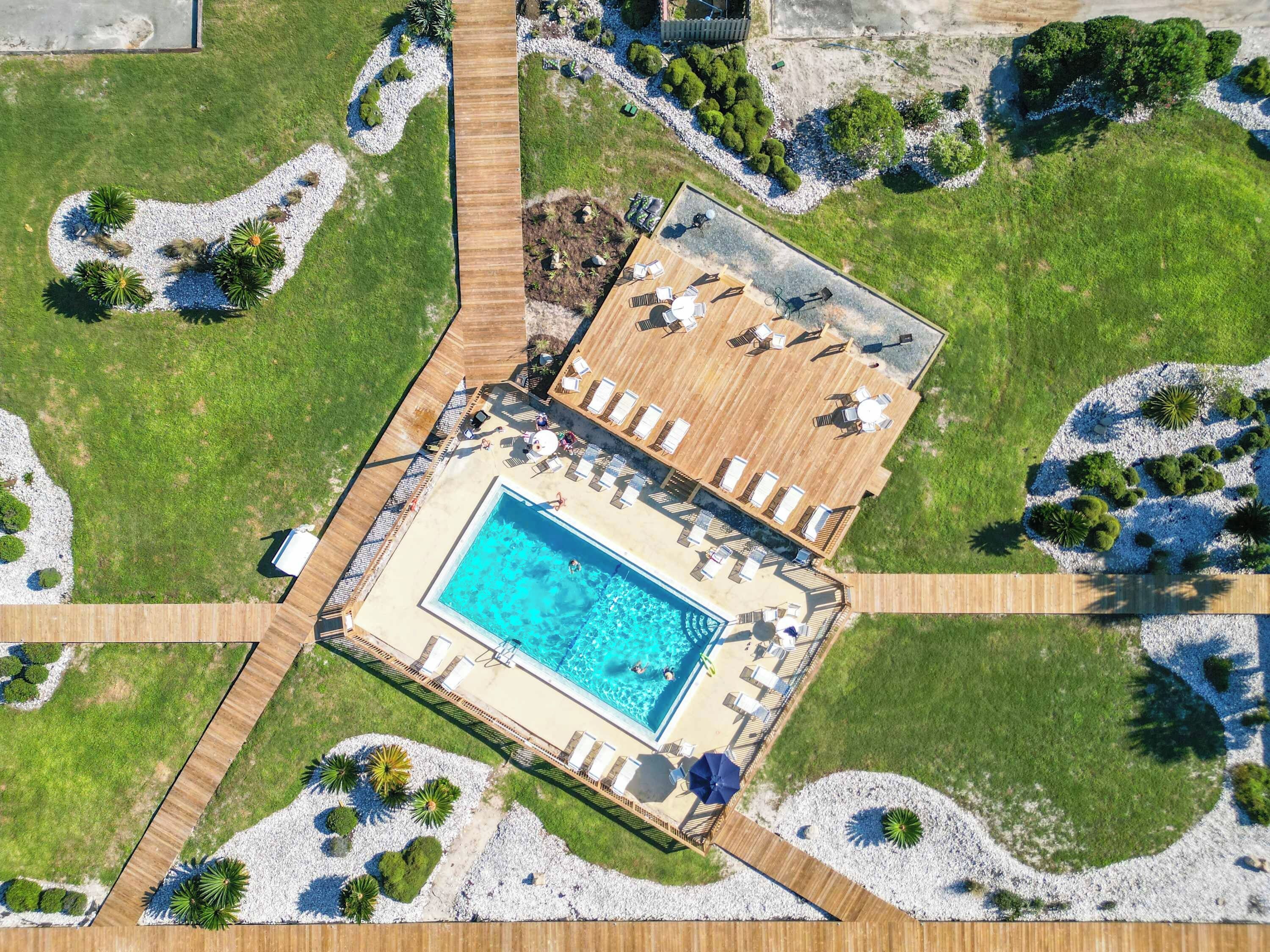 An aerial view of a resort with a swimming pool, sun loungers, and a wooden deck.