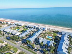 An aerial view of a coastal hotel with multiple buildings, a beach, and a swimming pool.