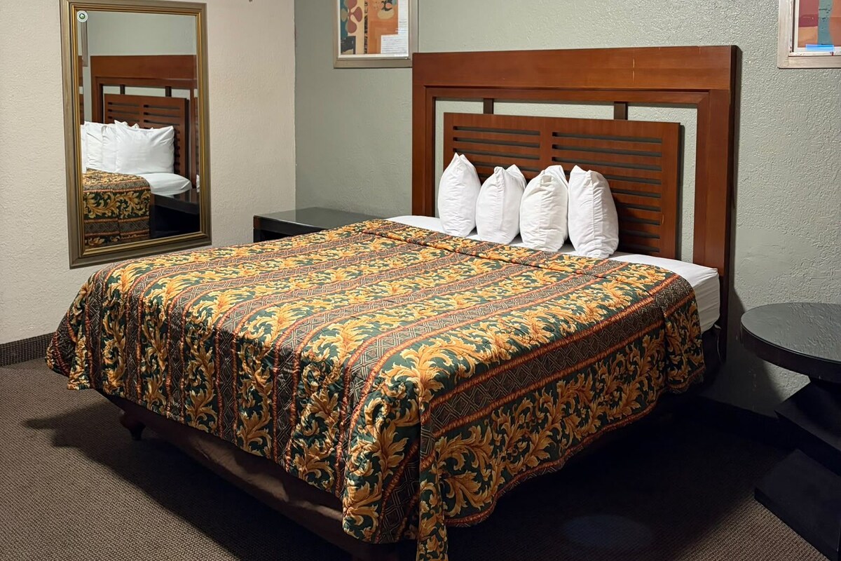Una habitación de hotel con una cama, una mesita de noche, un espejo y una obra de arte colgada en la pared.