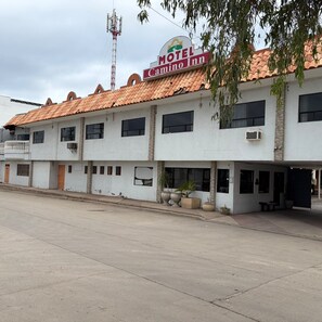 Un motel de dos pisos con techo de tejas, múltiples ventanas y zona de estar al aire libre.