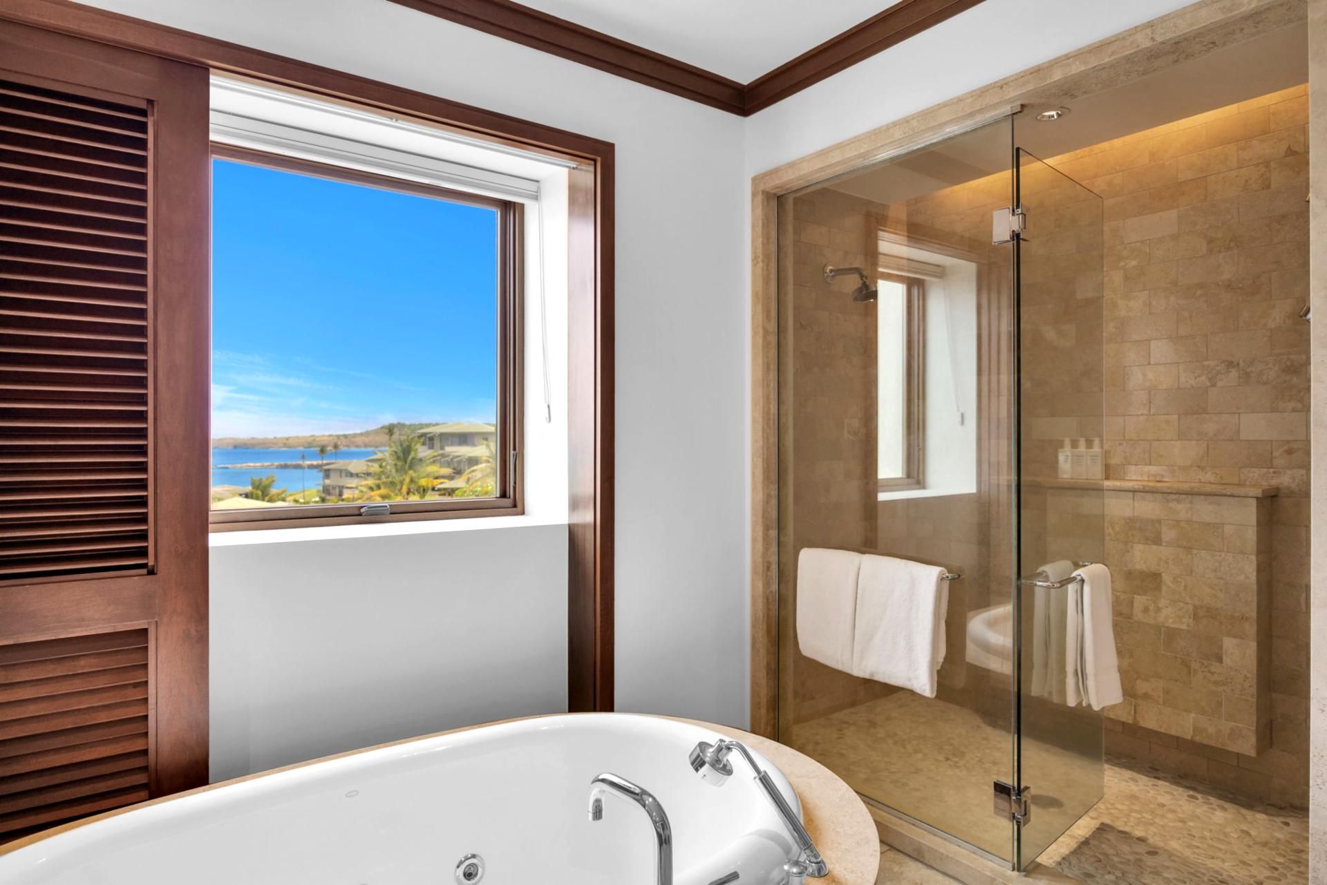 A bathroom with a bathtub, a glass-enclosed shower, and a view of a body of water through a window.
