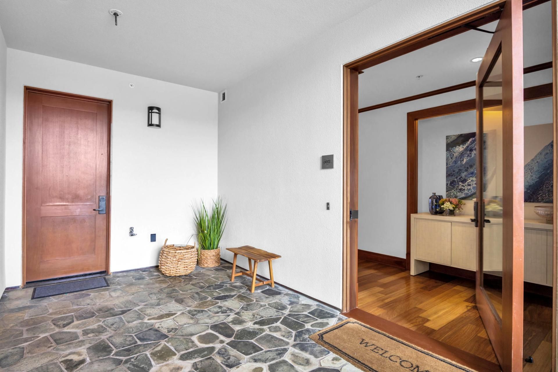 A stone-floored entrance with a wooden door, a small table, and a welcome mat.