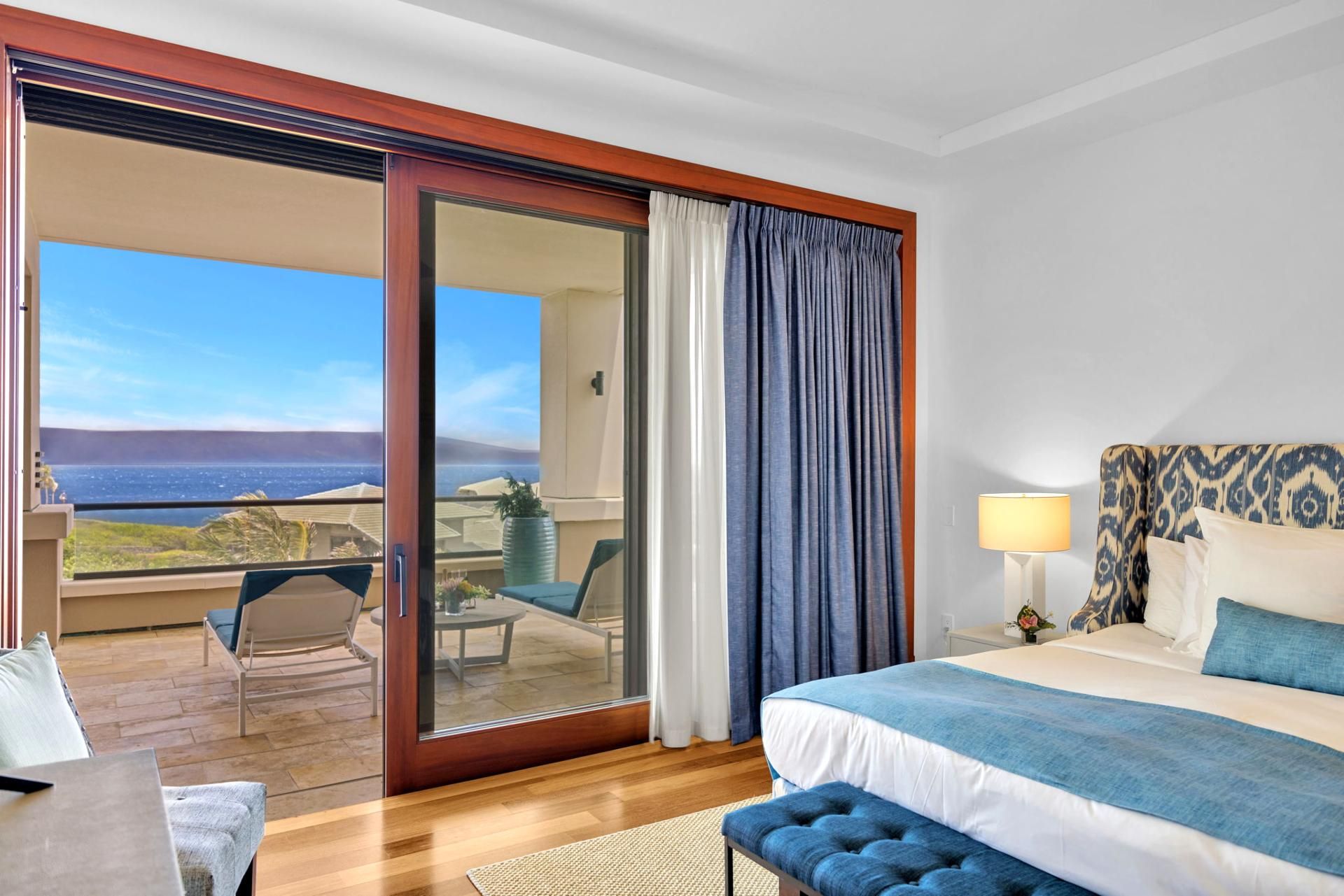 A hotel room with a bed, a desk, a chair, a lamp, and a view of the ocean.