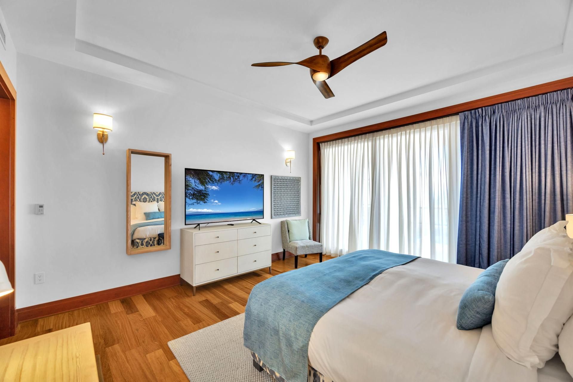 A bedroom with a bed, a TV, a dresser, and a ceiling fan.