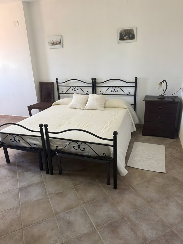 A bedroom with a bed, a chair, a nightstand, and a rug. - Room 'Tripla Standard 1' with Shared Terrace, Wi-Fi and Air Conditioning (Nulvi)