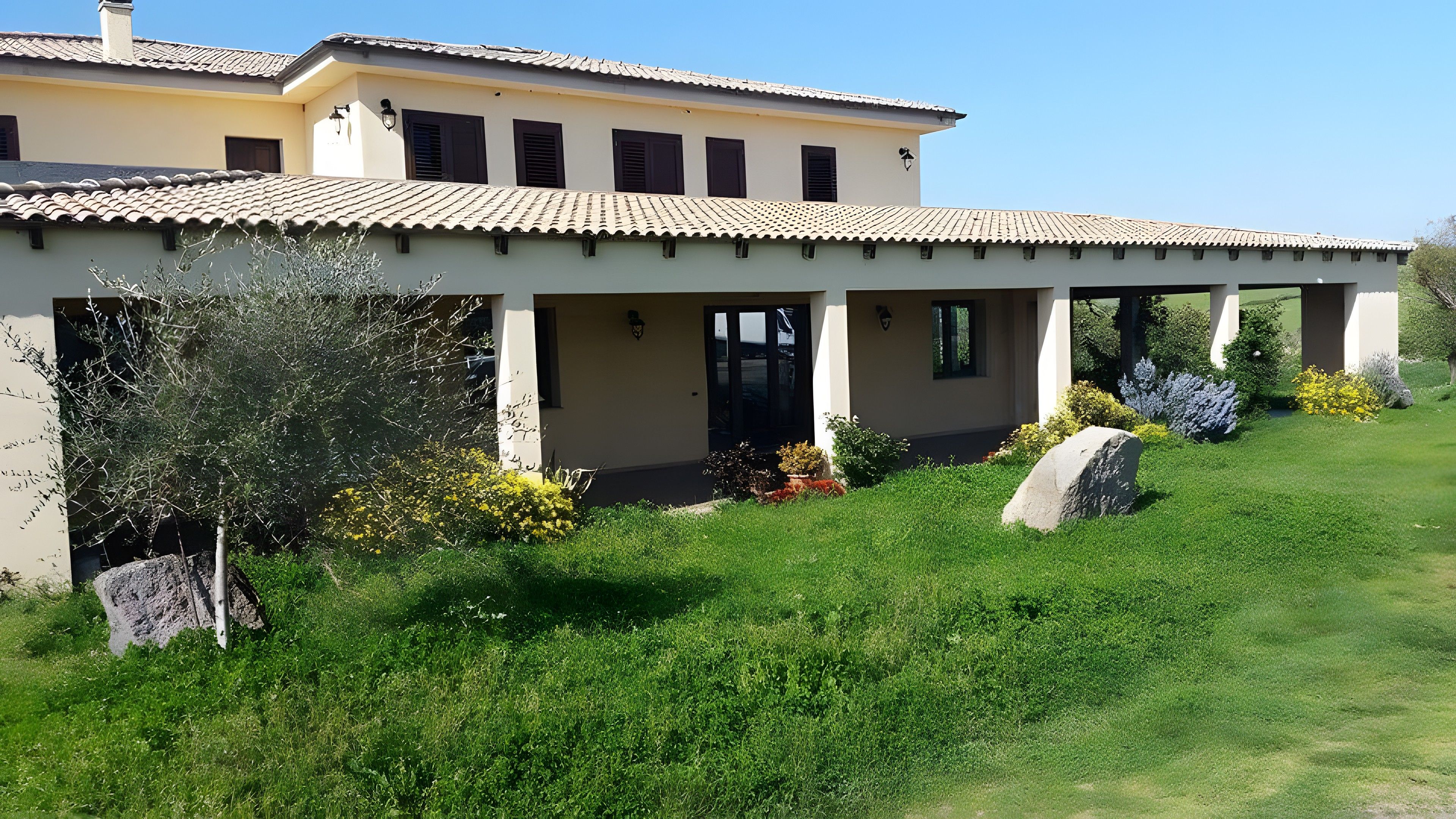 A two-story building with a tiled roof, a covered patio area, and a well-maintained garden with rocks and shrubs.