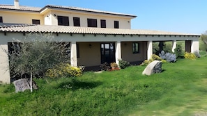 A two-story building with a tiled roof, a covered patio area, and a well-maintained garden with rocks and shrubs. - Room 'Camera Tripla Standard 3' with Shared Terrace, Wi-Fi and Air Conditioning (Nulvi)