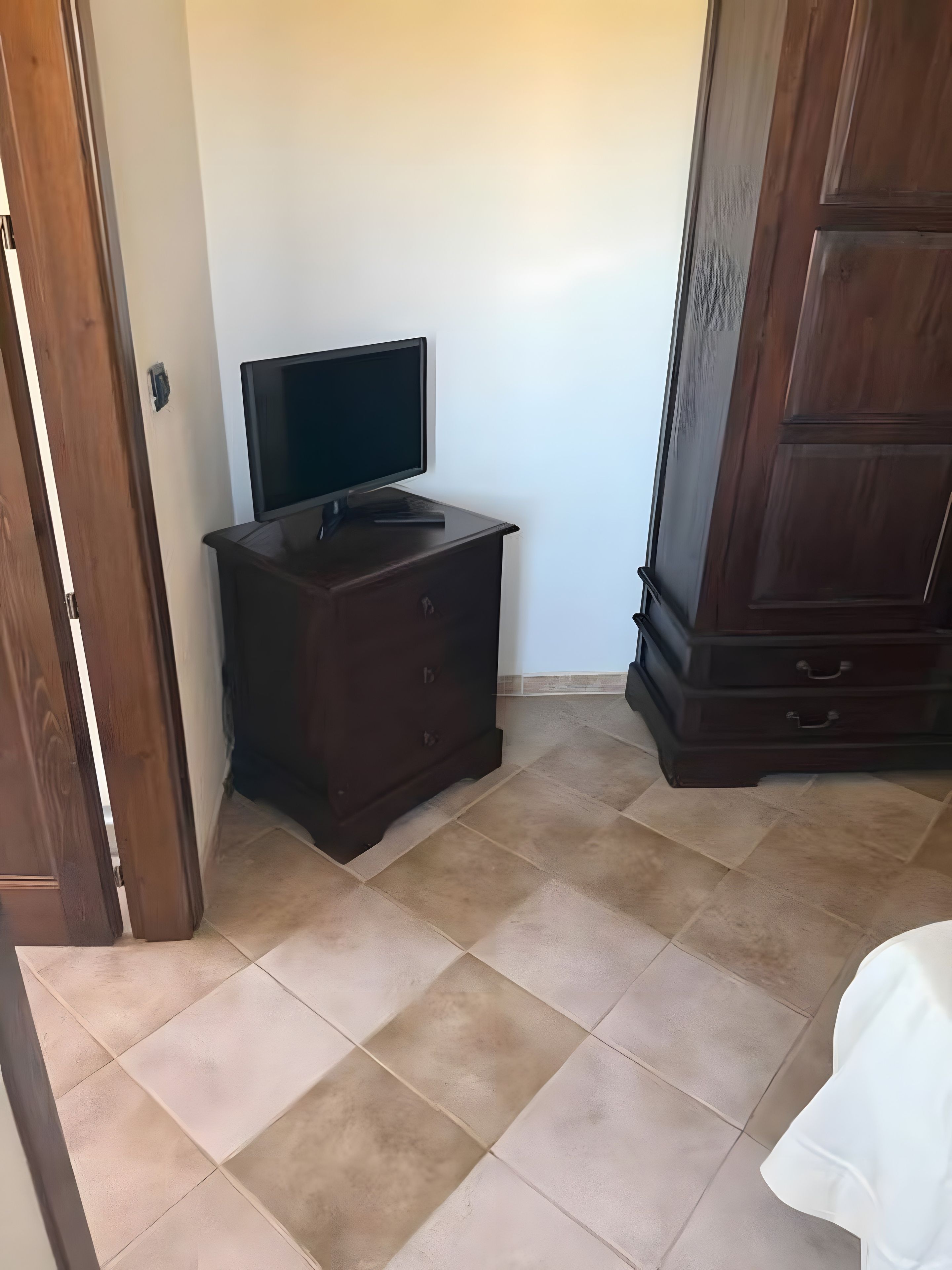 Ein Zimmer mit einem dunklen Holzschrank, einem Fernseher darauf und einem gefliesten Boden.