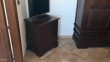 Ein Zimmer mit einem dunklen Holzschrank, einem Fernseher darauf und einem gefliesten Boden.
