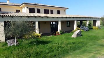 A two-story building with a tiled roof, a covered patio area, and a well-maintained garden with rocks and shrubs.