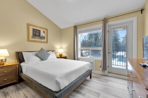 A bedroom with a bed, bedside tables, a dresser, a window with a view of trees, and a door. - B243- Cozy 2-bedroom townhome in wonderful Harvie Heights with AC (Harvie Heights)